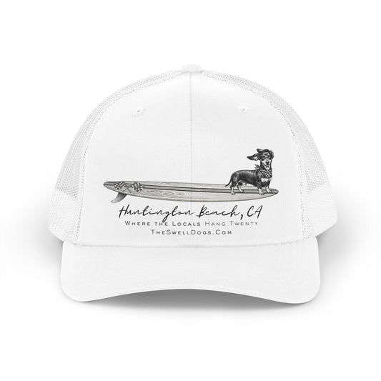 White trucker hat featuring a Dachshund dog standing on a surfboard with "Huntington Beach, CA" text