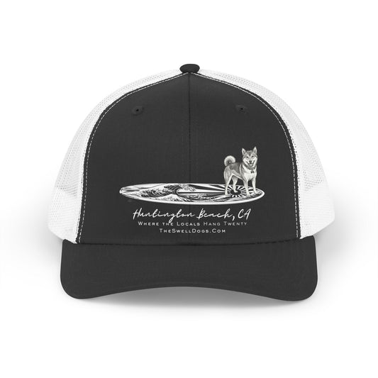 Black trucker hat featuring a Shiba Inu dog standing on a Japanese surfboard with "Huntington Beach, CA" text