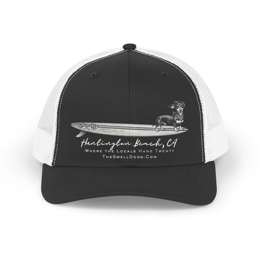 Trucker hat featuring a Dachshund dog standing on a surfboard with "Huntington Beach, CA" text