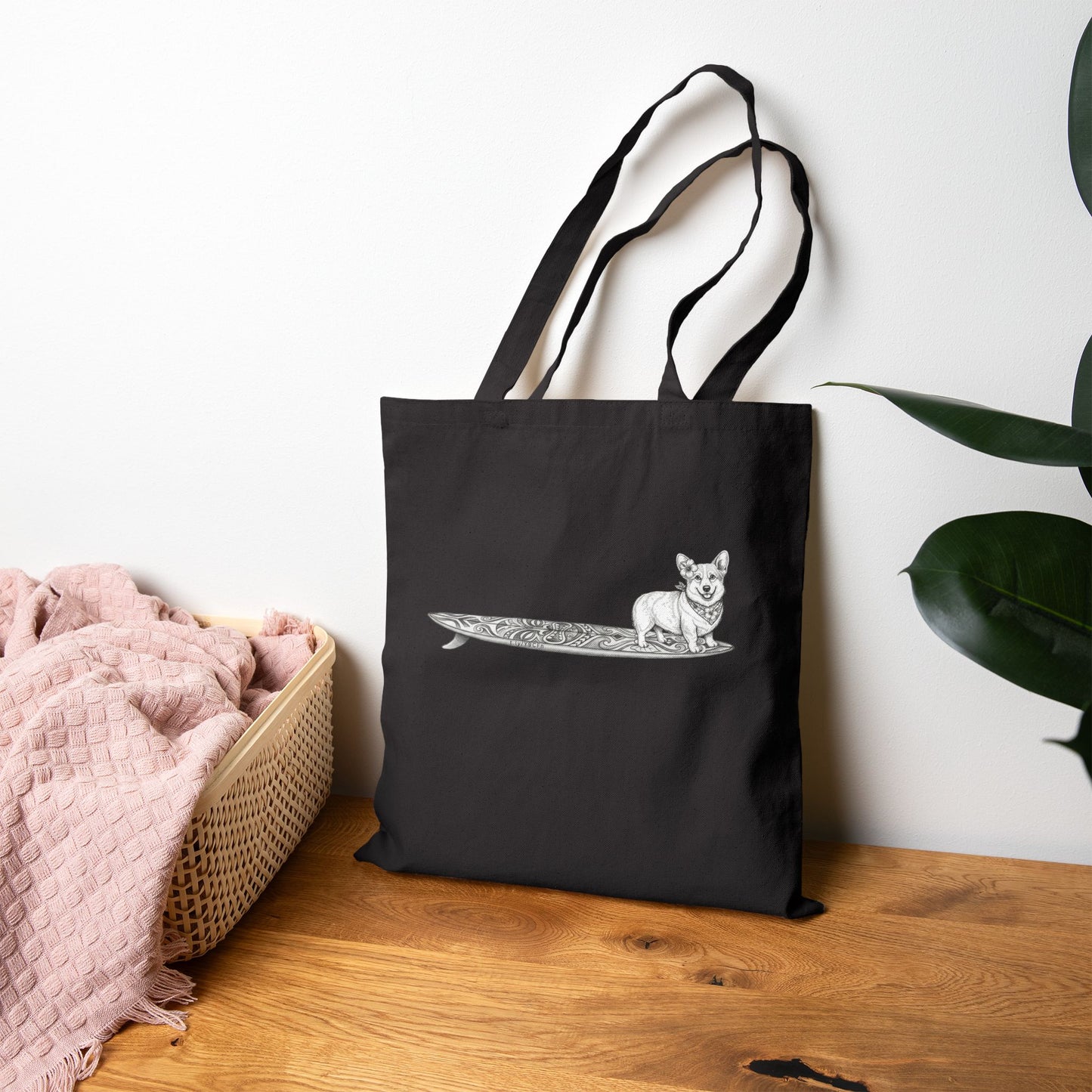 Black Corgi surf tote bag with hibiscus bandana tiki surfboard illustration styled on wooden surface with pink blanket — The Swell Dogs