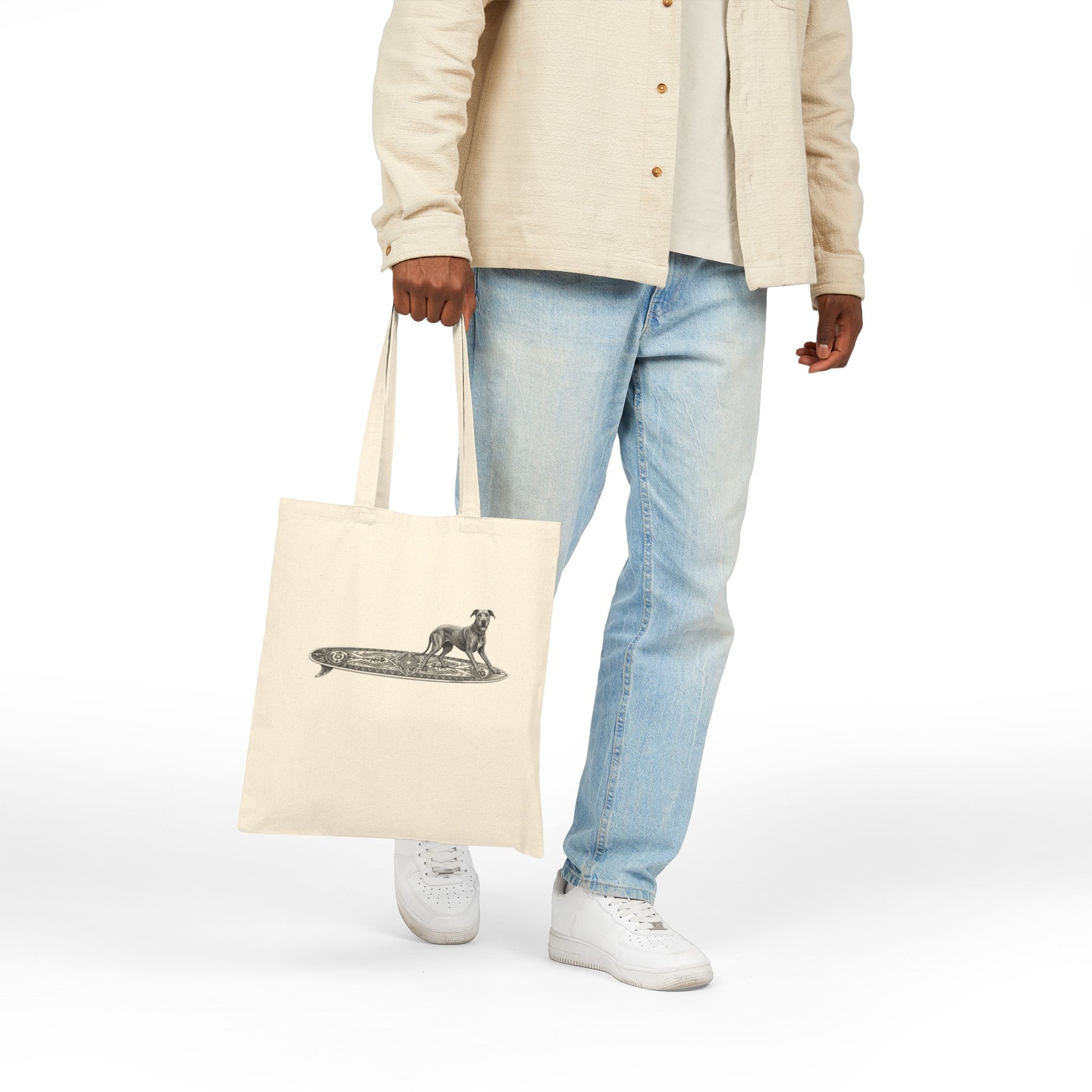 Person holding a beige  tote bag with a Great Dane on a longboard with wild boar crests and suns on it.