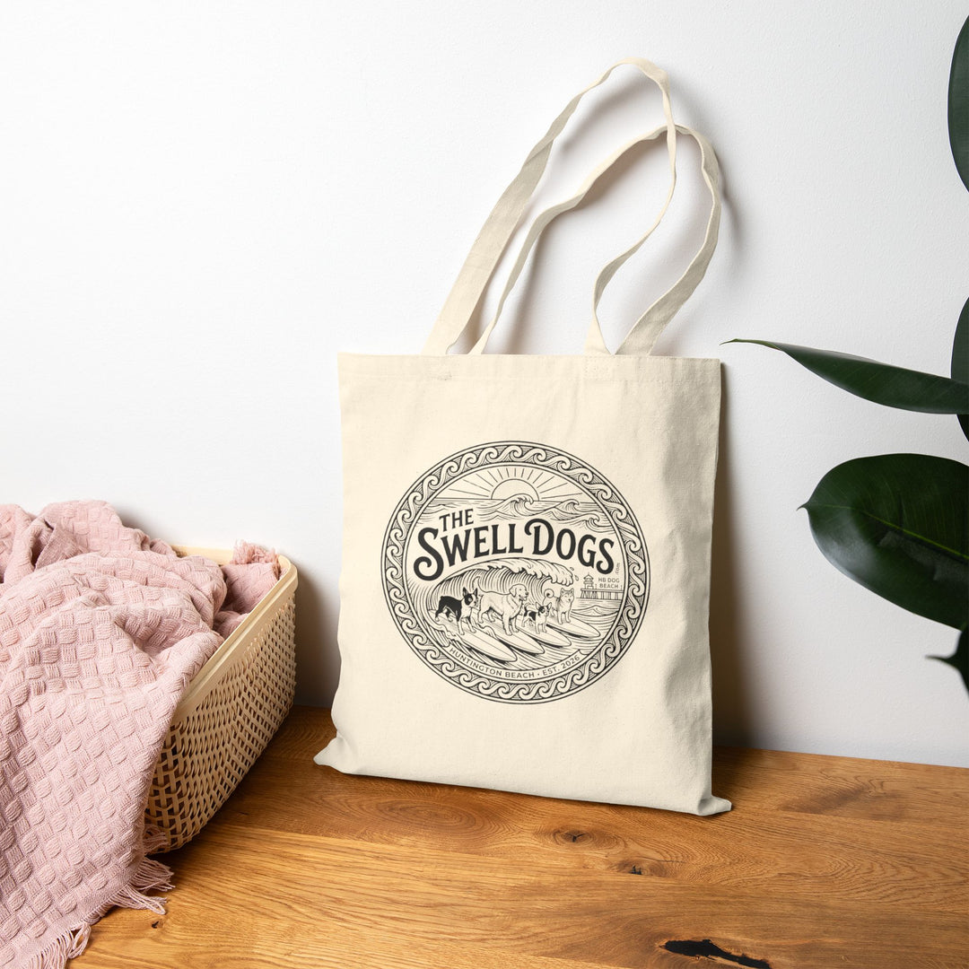 Beige tote bag with a Swell Dogs logo on a wood floor.