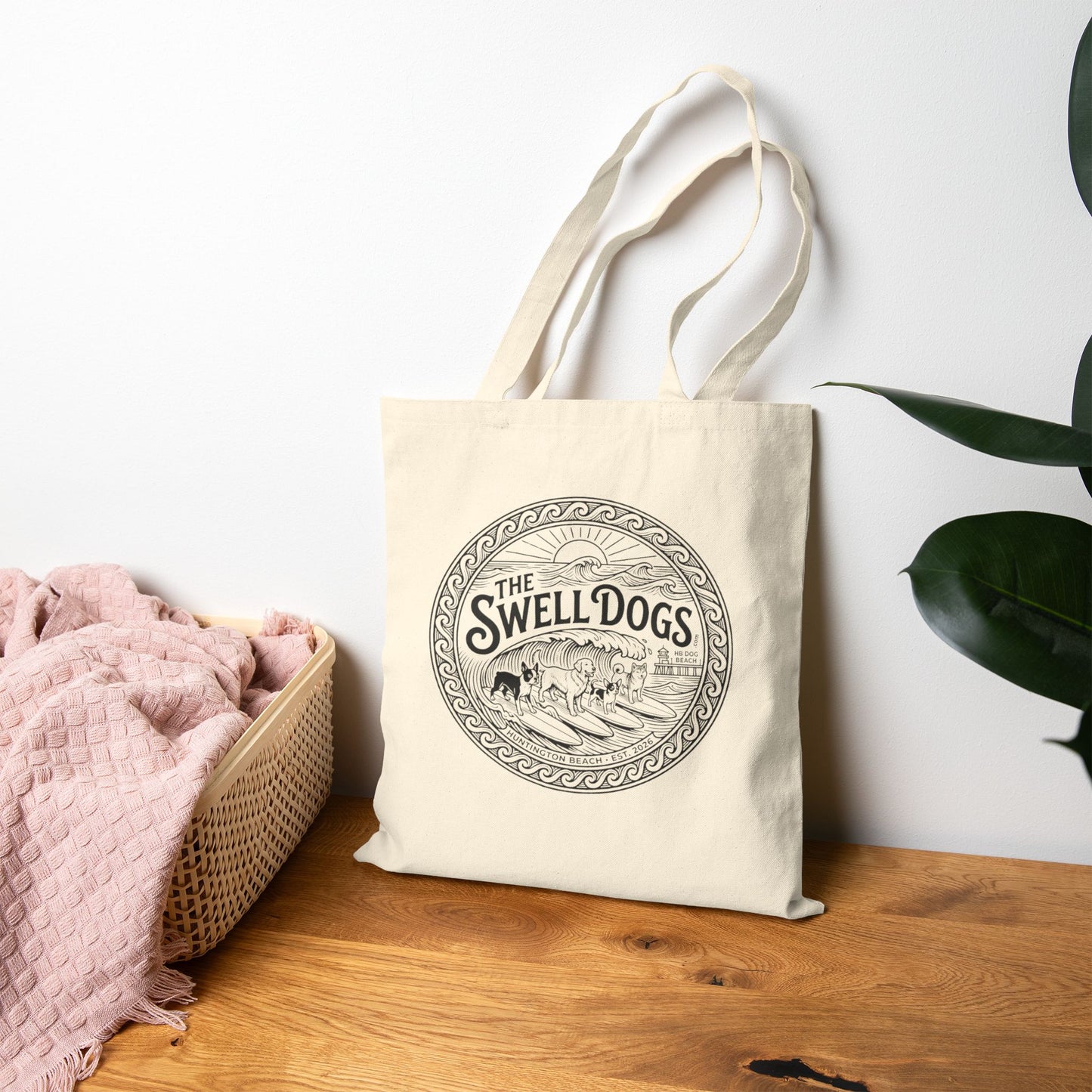 Beige tote bag with a Swell Dogs logo on a wood floor.
