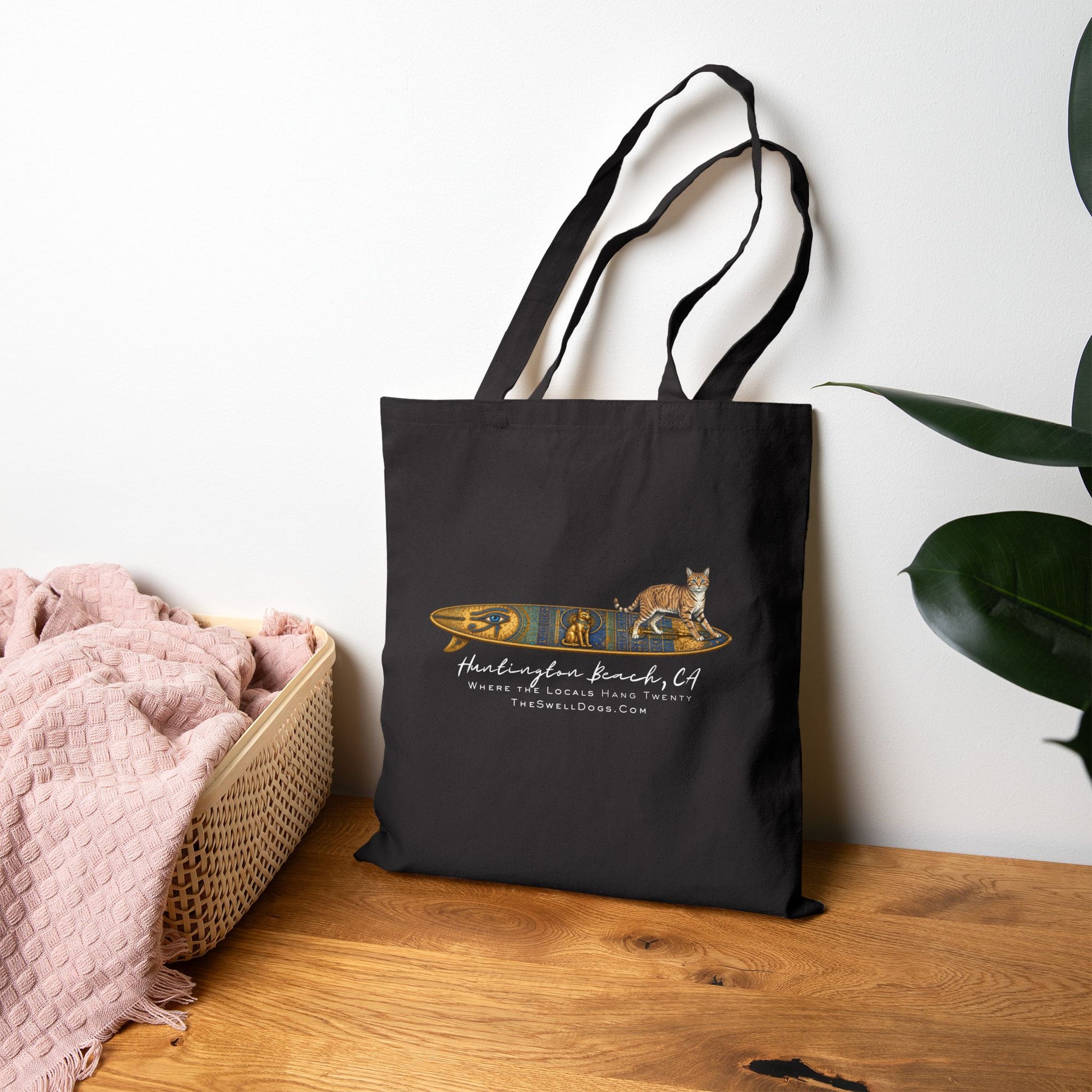 Black tote bag featuring a tabby cat standing on an Egyptian surfboard with "Huntington Beach, CA" text