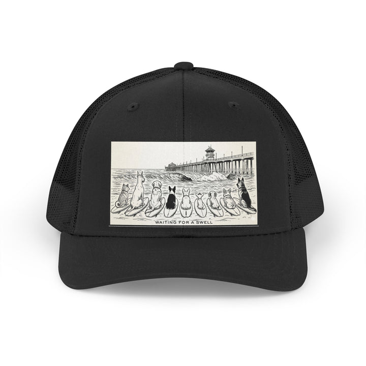 Black trucker hat with a picture of a pack of nine dogs sitting on their surfboards, facing the ocean, with the Huntington Beach pier in the background. It says Waiting for a Swell at the bottom.