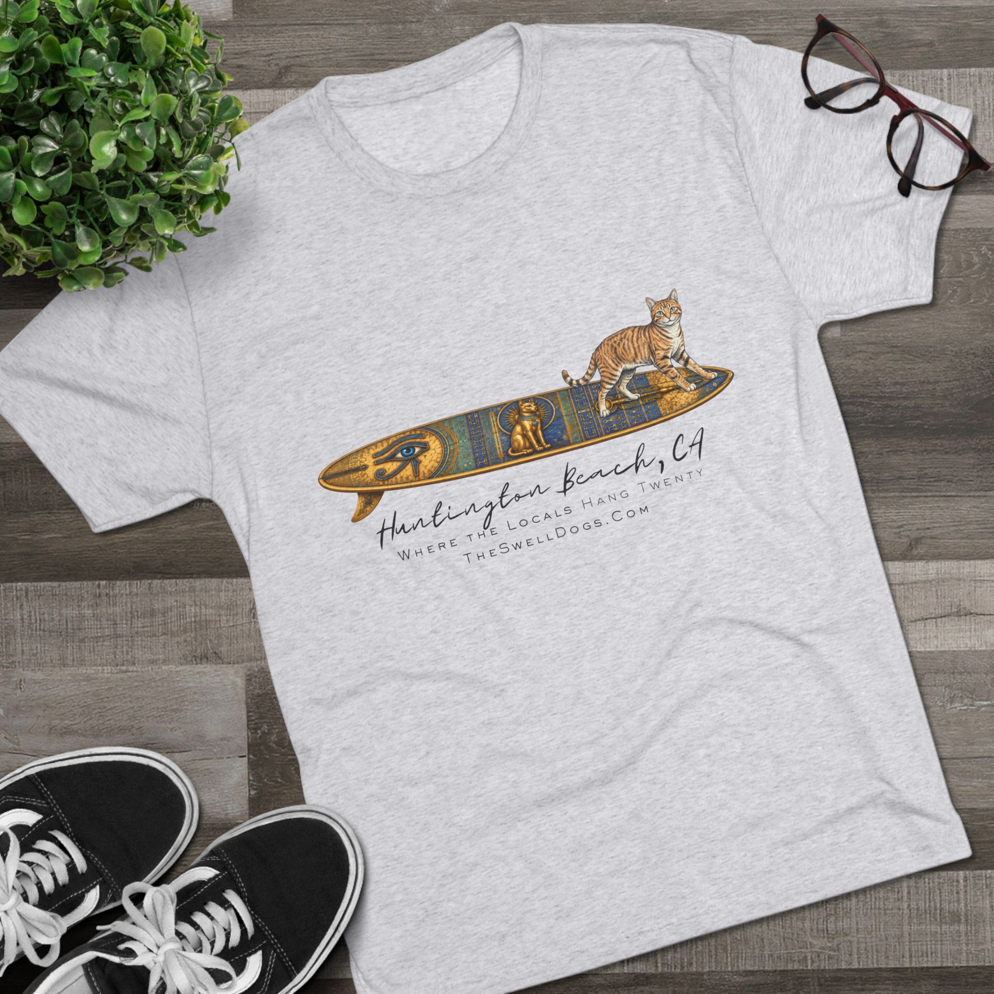 White t-shirt featuring a tabby cat standing on an Egyptian surfboard with "Huntington Beach, CA" text