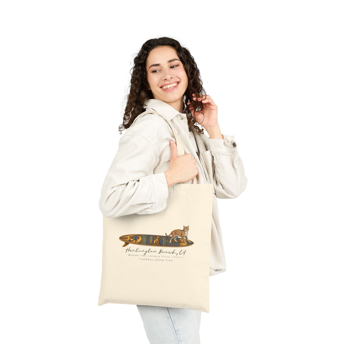 Girl carrying a biege tote bag featuring a tabby cat standing on an Egyptian surfboard with "Huntington Beach, CA" text