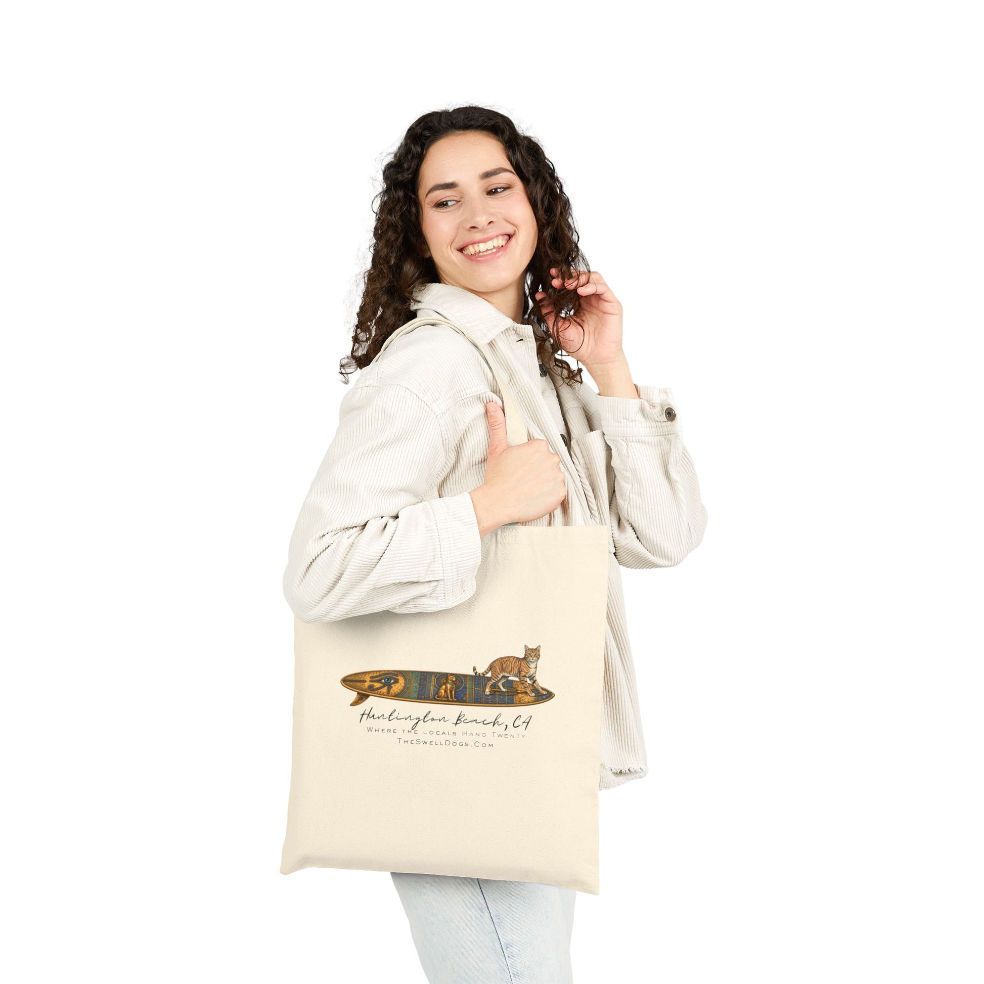 Girl carrying a biege tote bag featuring a tabby cat standing on an Egyptian surfboard with "Huntington Beach, CA" text