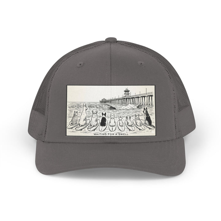 Gray trucker hat with a picture of a pack of nine dogs sitting on their surfboards, facing the ocean, with the Huntington Beach pier in the background. It says Waiting for a Swell at the bottom.
