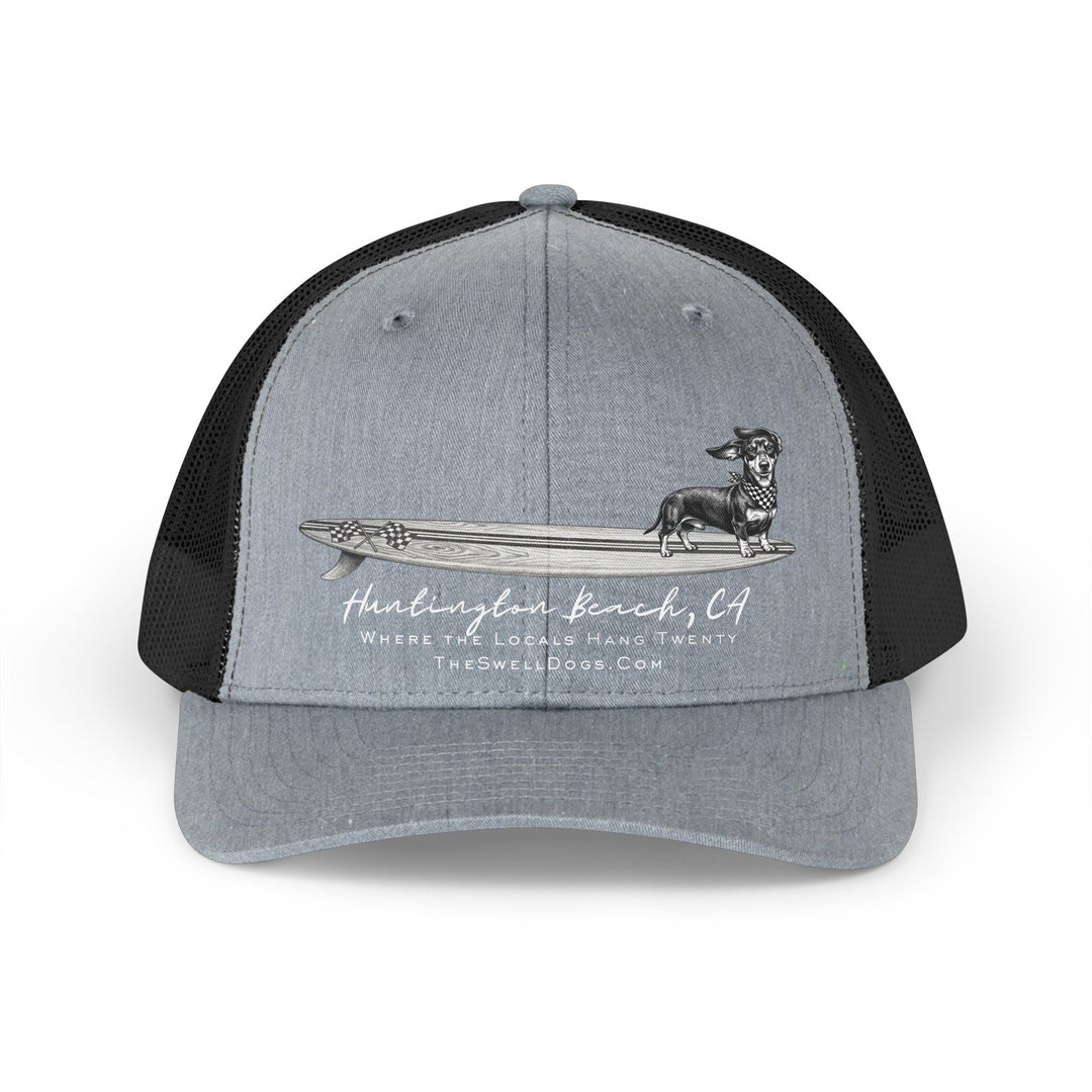 Grey and black trucker hat featuring a Dachshund dog standing on a surfboard with "Huntington Beach, CA" text