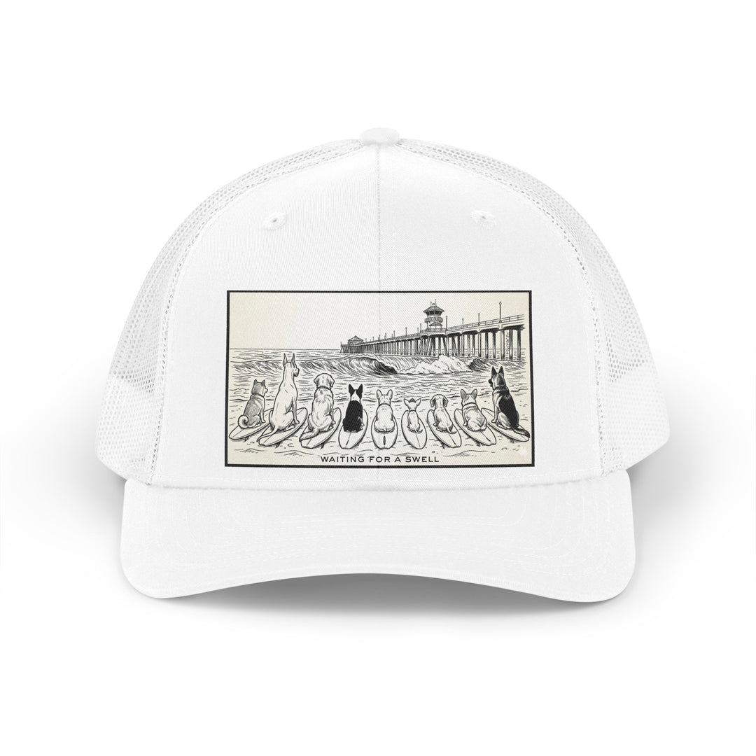 White trucker hat with a picture of a pack of nine dogs sitting on their surfboards, facing the ocean, with the Huntington Beach pier in the background. It says Waiting for a Swell at the bottom.