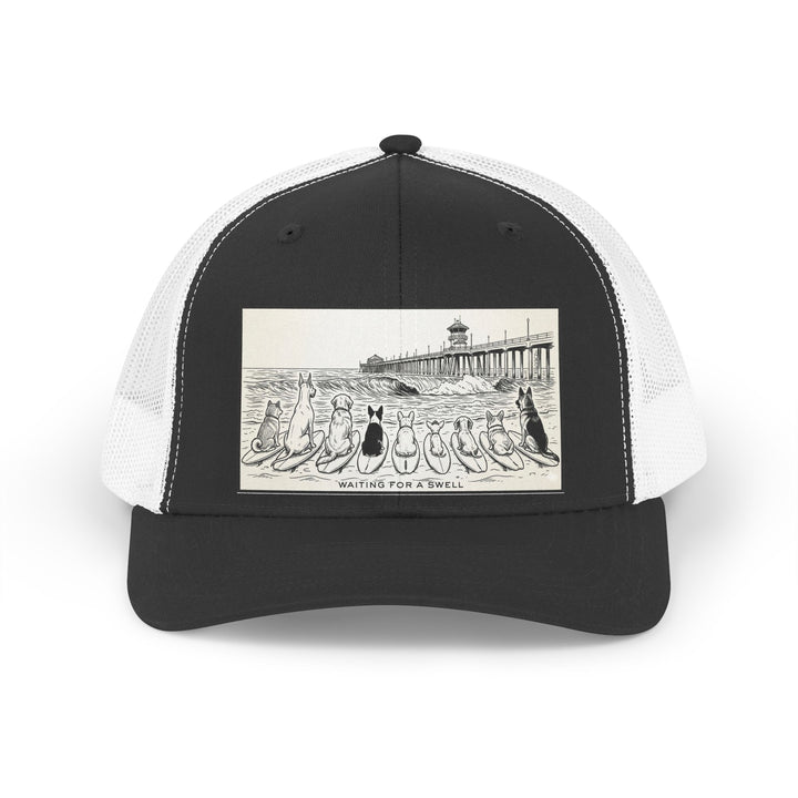 Black and white trucker hat with a picture of a pack of nine dogs sitting on their surfboards, facing the ocean, with the Huntington Beach pier in the background. It says Waiting for a Swell at the bottom.