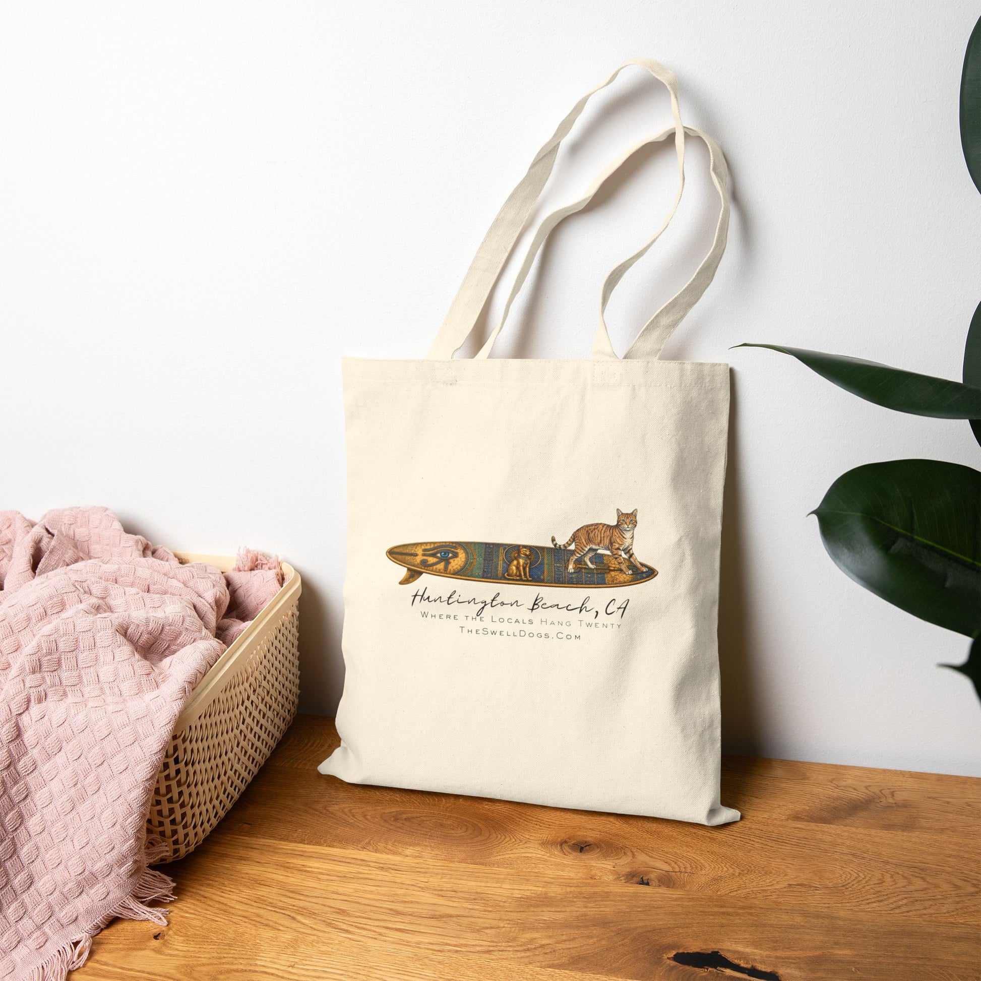 Biege tote bag featuring a tabby cat standing on an Egyptian surfboard with "Huntington Beach, CA" text
