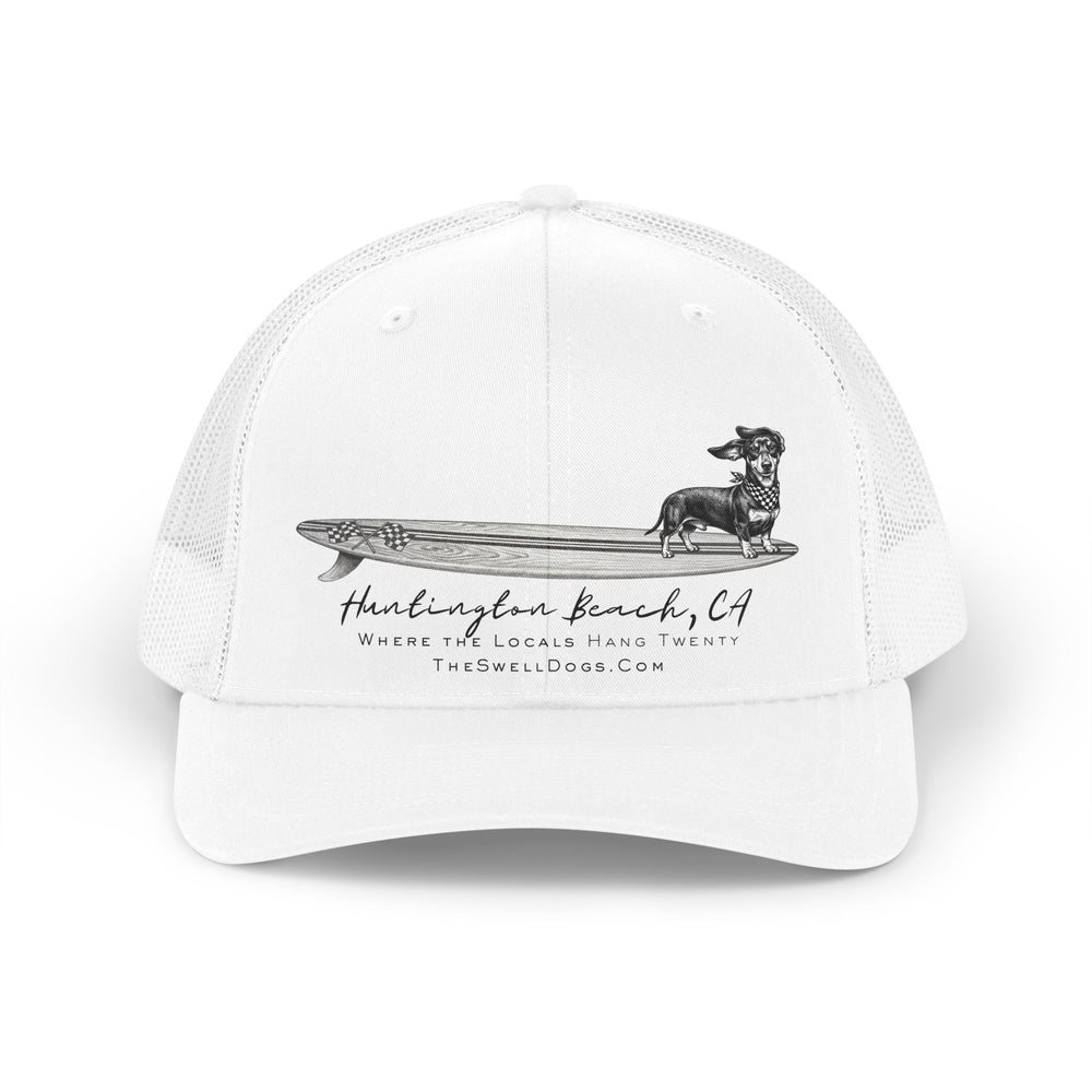 White trucker hat featuring a Dachshund dog standing on a surfboard with "Huntington Beach, CA" text