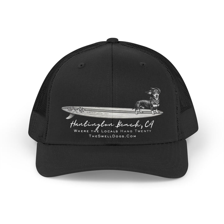 Black trucker hat featuring a Dachshund dog standing on a surfboard with "Huntington Beach, CA" text