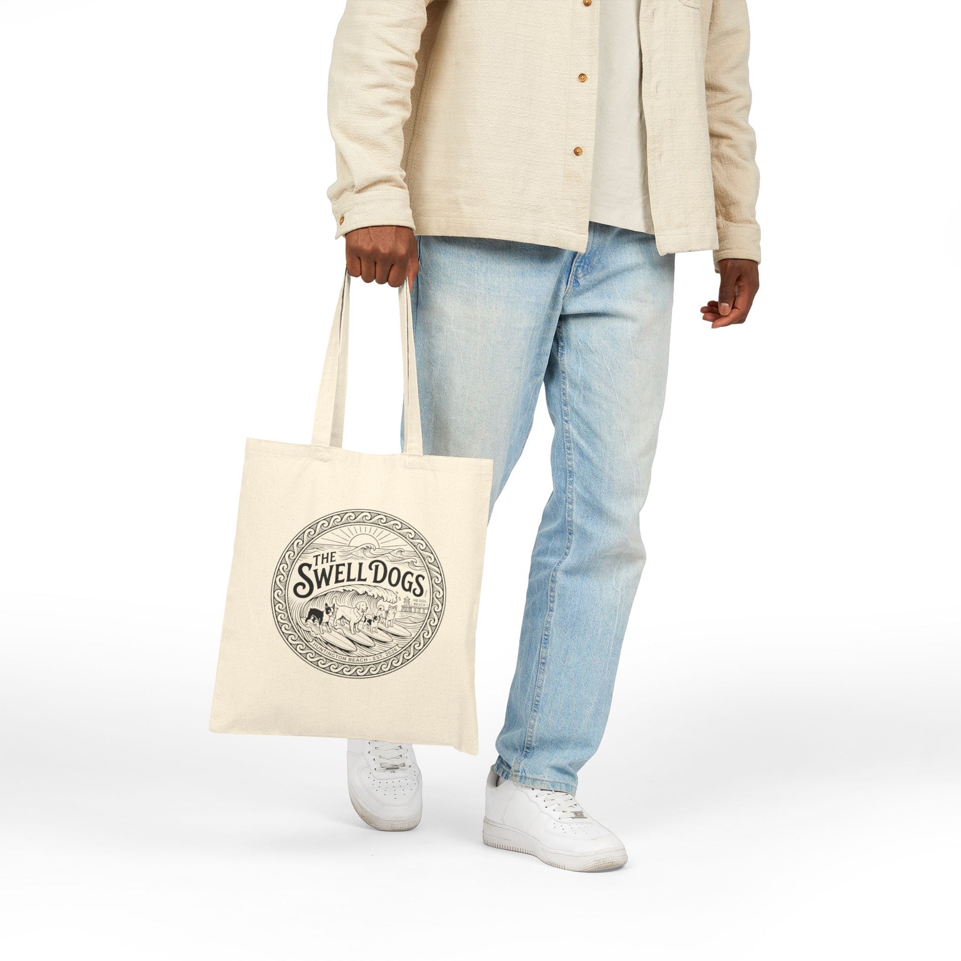 Person holding a beige tote bag with a Swell Dogs logo.