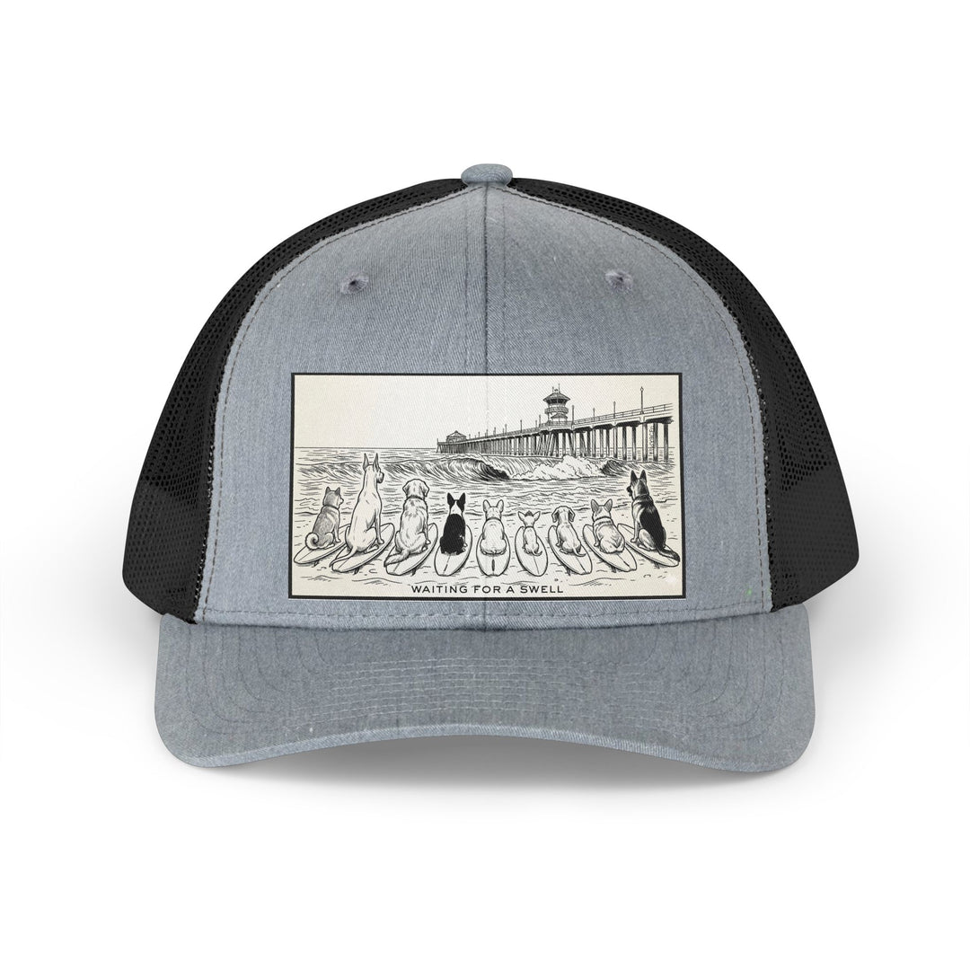 Gray and black trucker hat with a picture of a pack of nine dogs sitting on their surfboards, facing the ocean, with the Huntington Beach pier in the background. It says Waiting for a Swell at the bottom.
