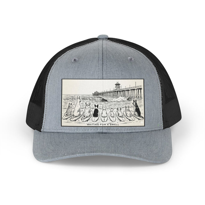 Gray and black trucker hat with a picture of a pack of nine dogs sitting on their surfboards, facing the ocean, with the Huntington Beach pier in the background. It says Waiting for a Swell at the bottom.