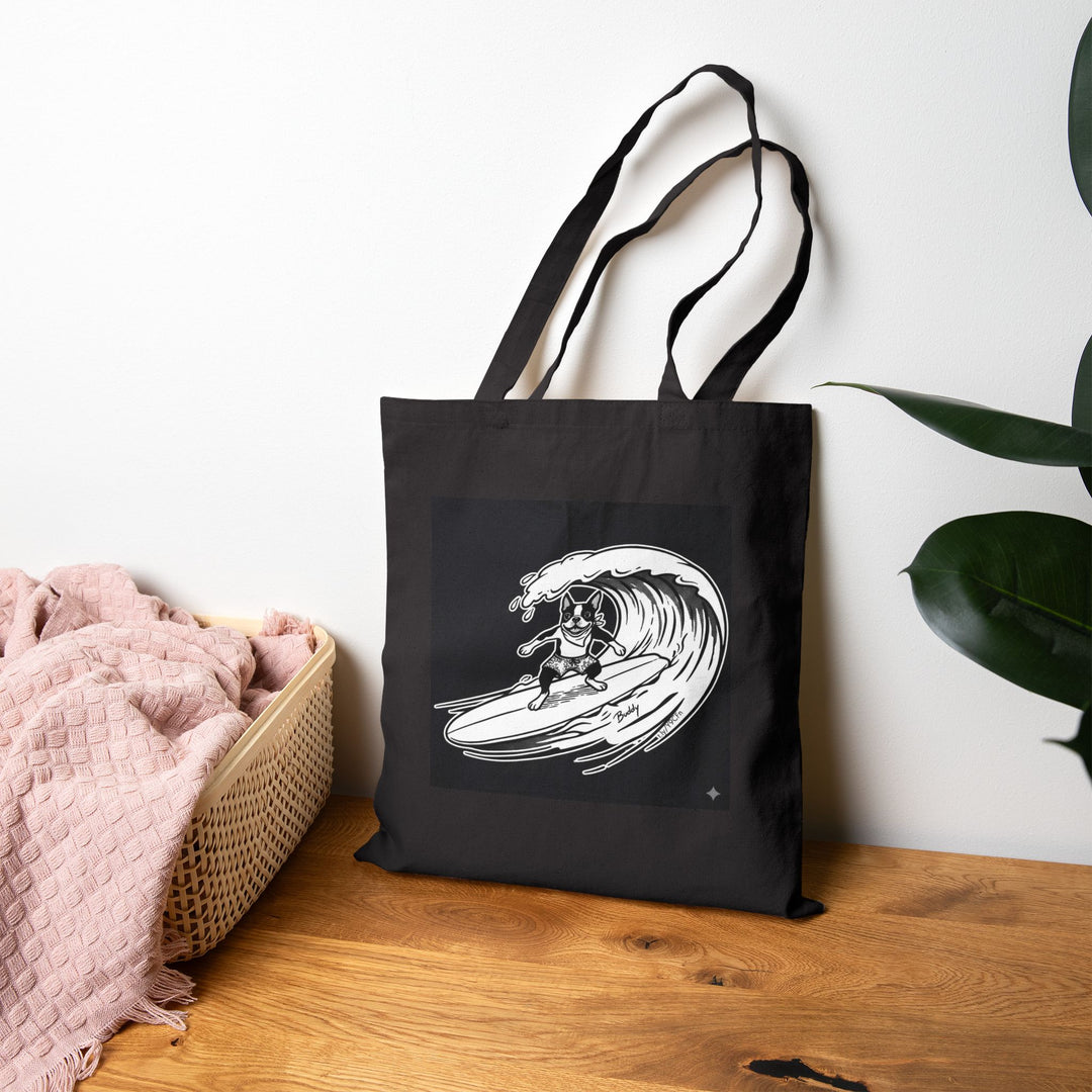Black tote bag with a graphic of a boston terrier riding a big wave on a longboard with a black background.