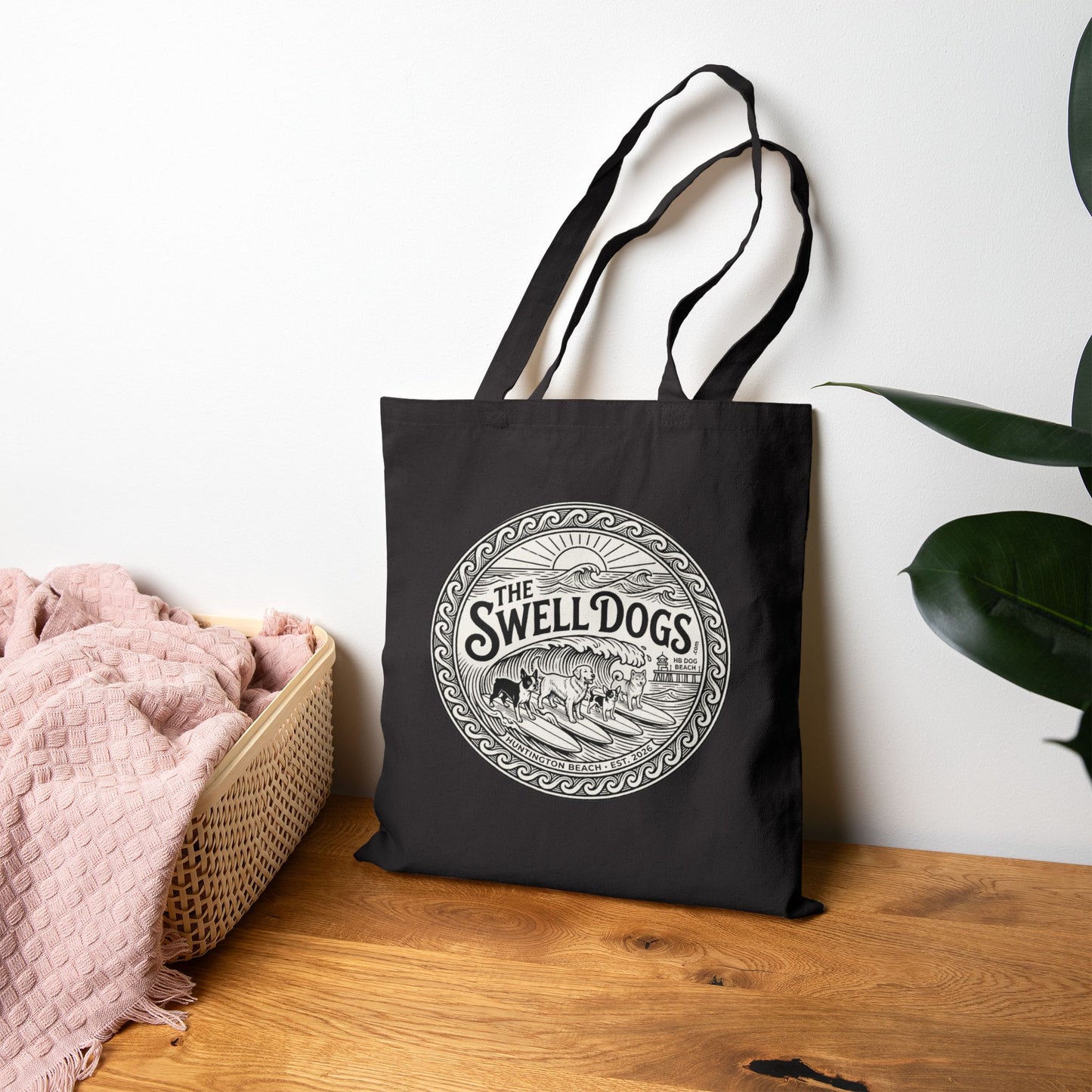 Black tote bag with a Swell Dogs logo on it on a wooden surface.