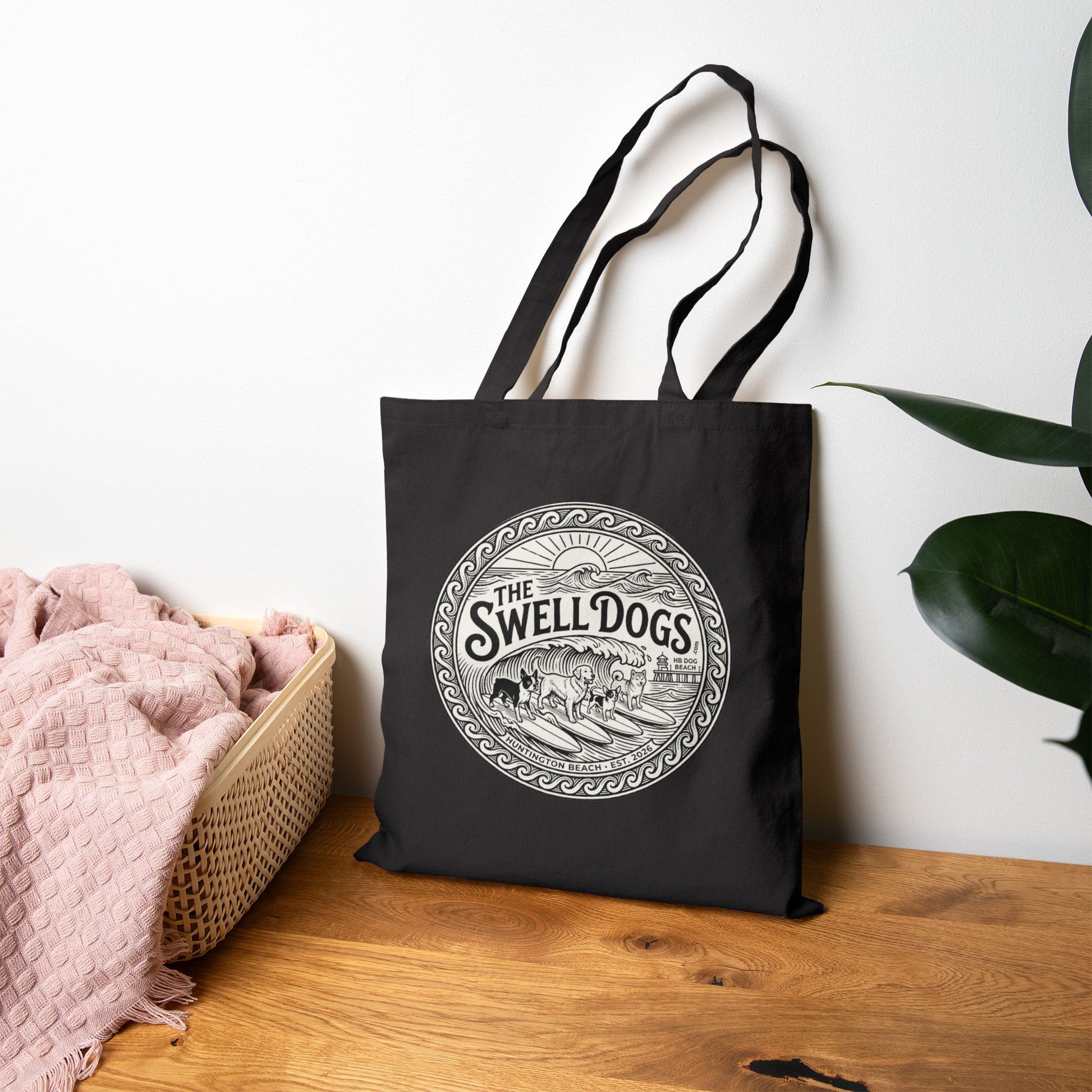 Black tote bag with a Swell Dogs logo on it on a wooden surface.