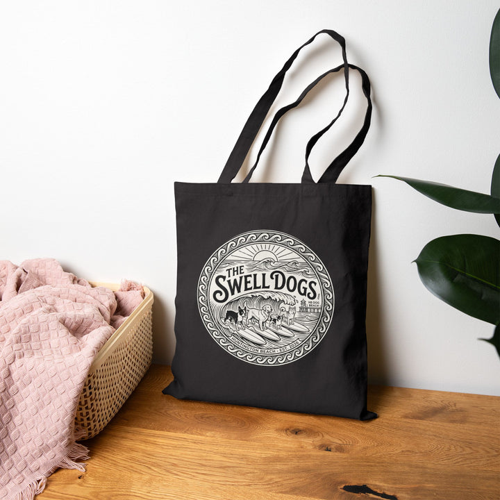 Black tote bag with a Swell Dogs logo on it on a wooden surface.