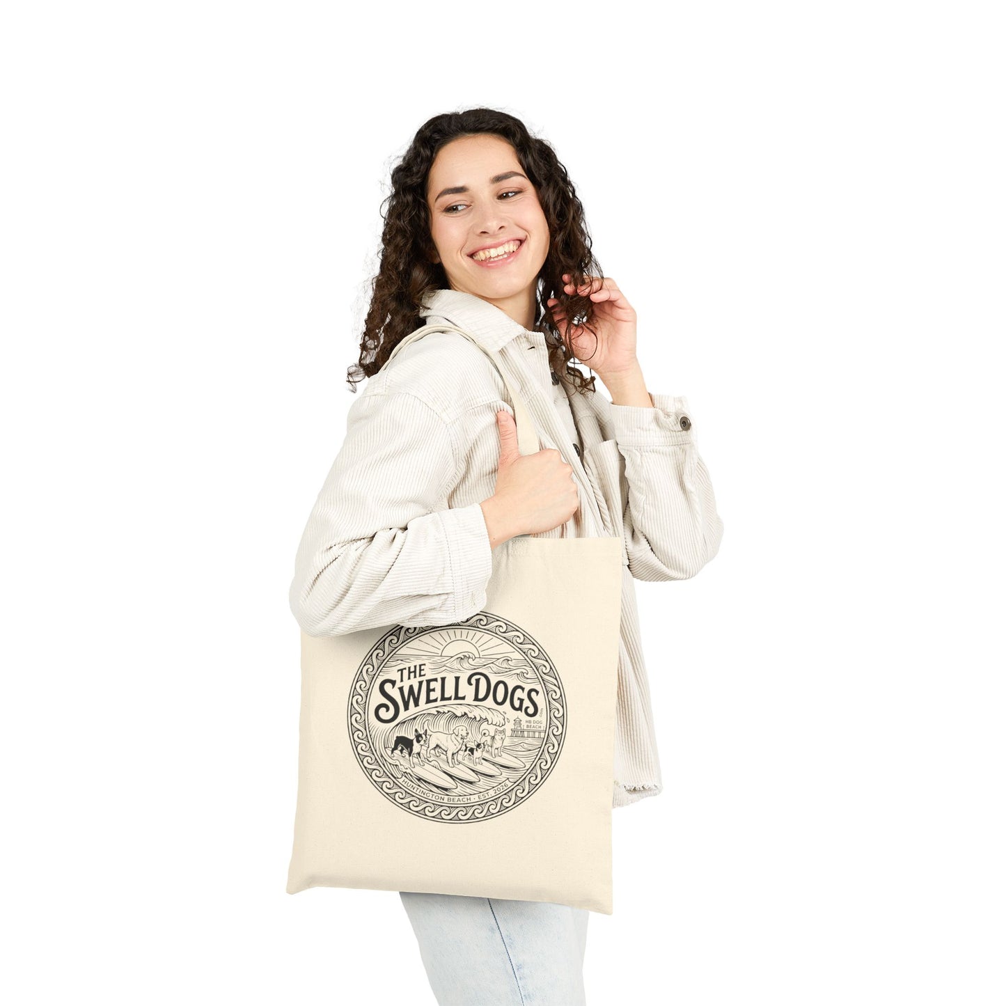Woman holding a beige tote bag with a Swell Dogs logo.