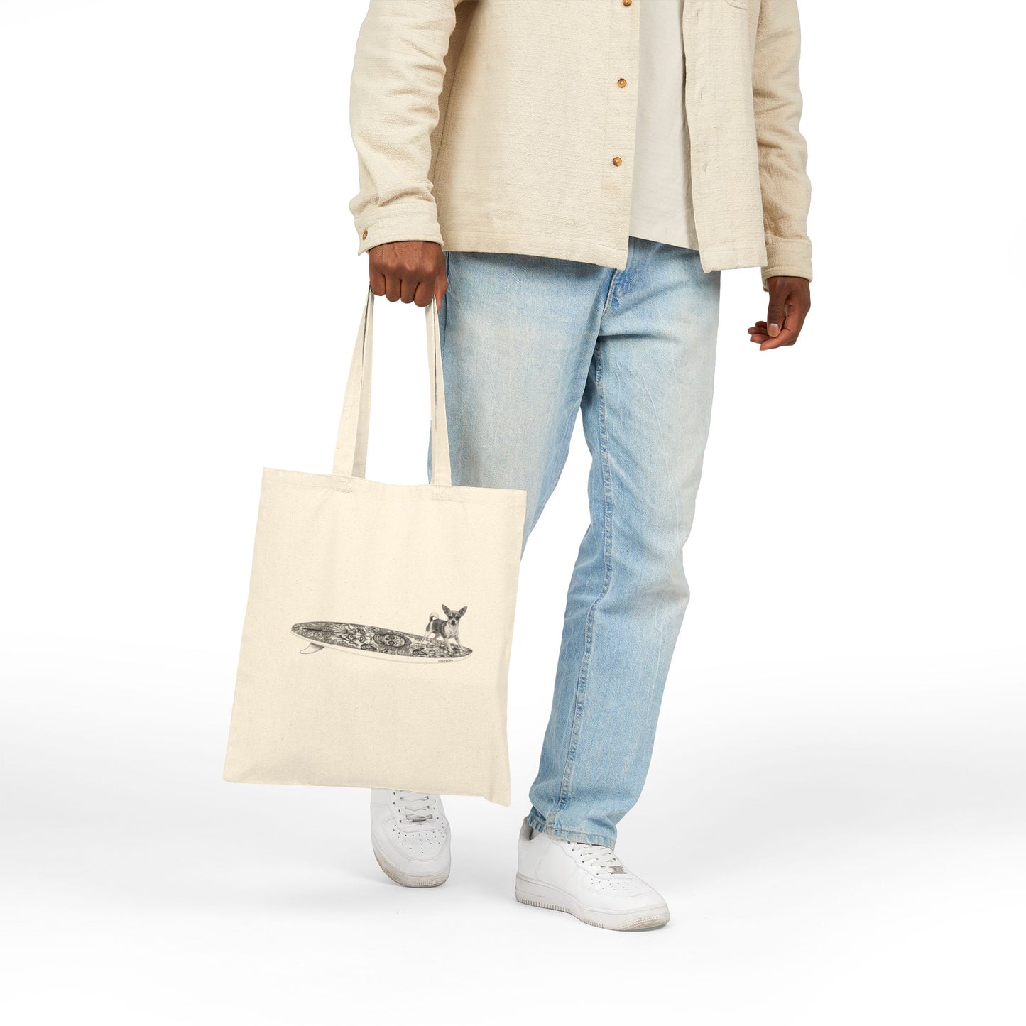 Person holding a beige tote bag with a Chihuahua surfing on a Day of the Dead surfboard.